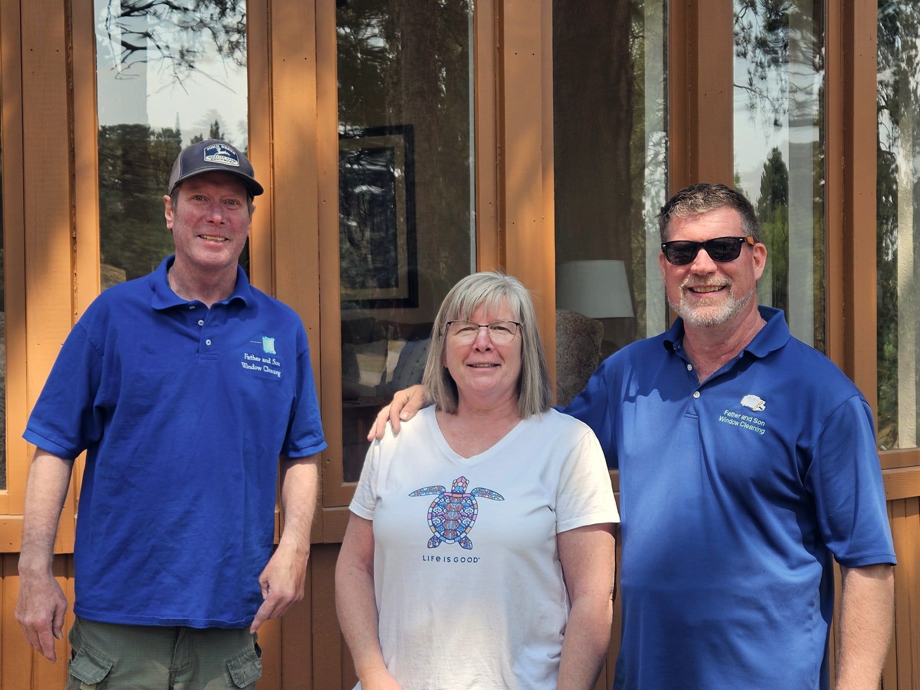 Two of the crew in branded polo shirts standing with a homeowner outside her front door, its glass panels freshly cleaned.