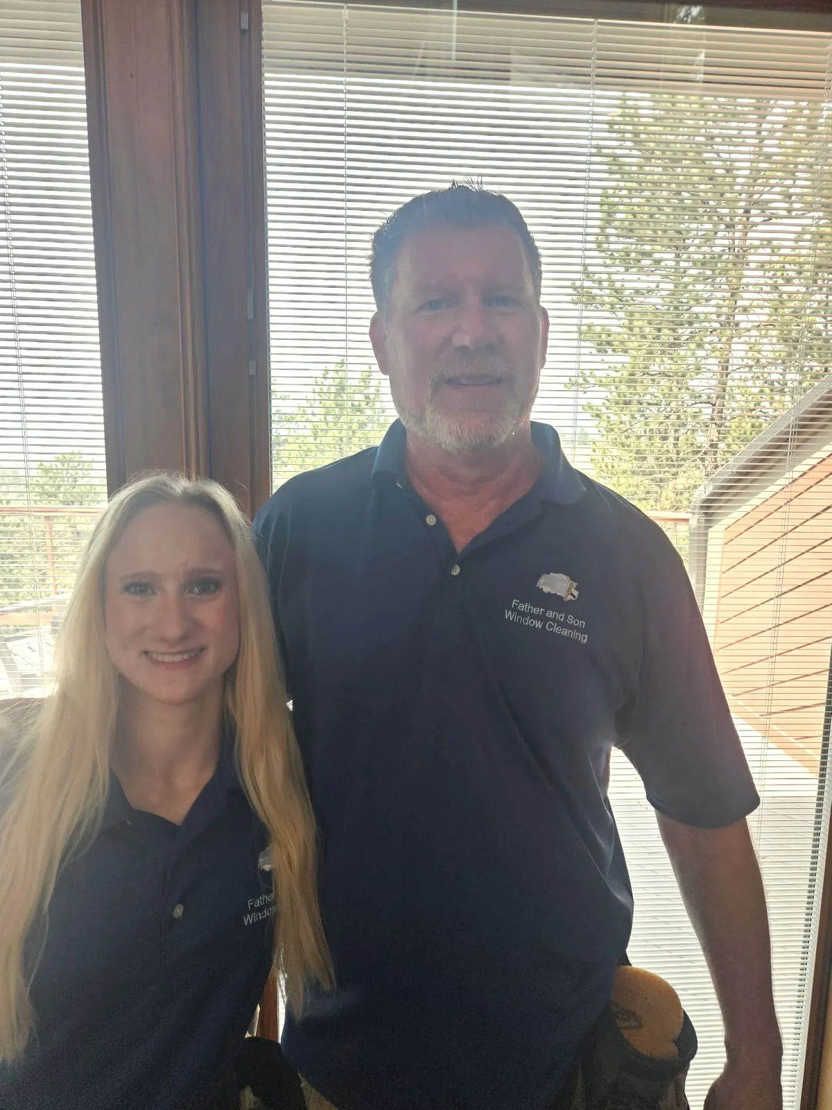 Two of the crew in branded polo shirts, standing together in front of a window inside a home they have just cleaned.