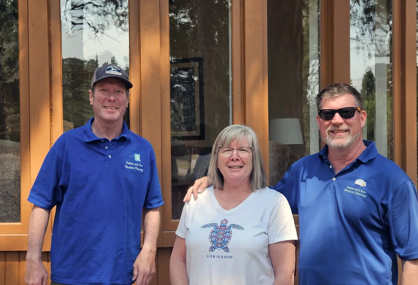 Three of the crew in branded Father & Son polo shirts, standing together in front of a home's freshly cleaned entry glass.