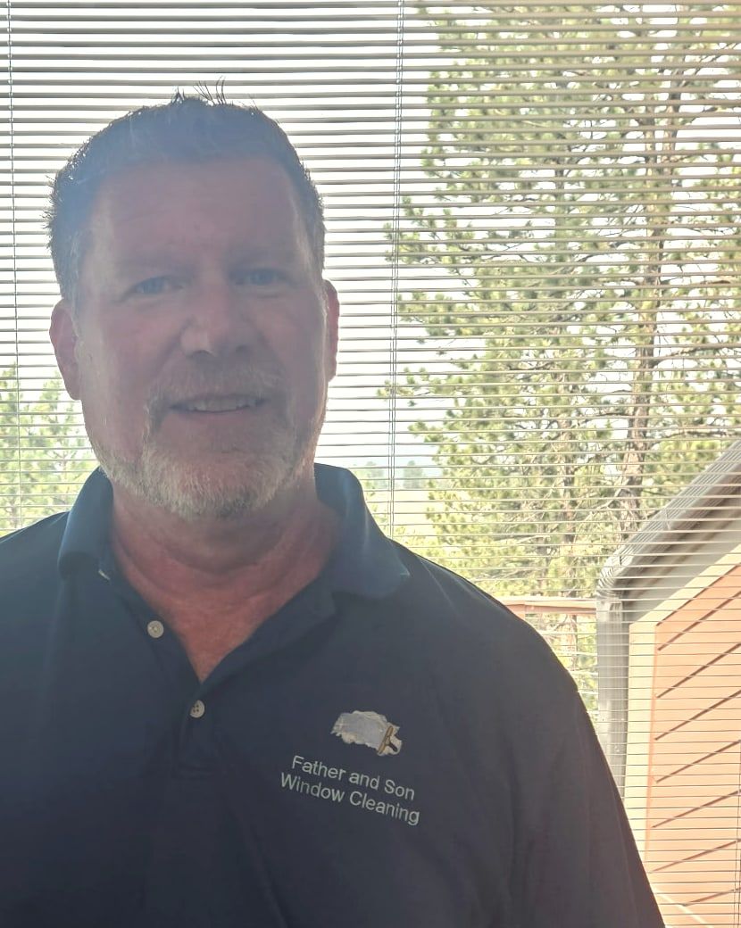Dan, owner and operator of Father & Son Window Cleaning, in a branded polo shirt beside a window in a foothills home.