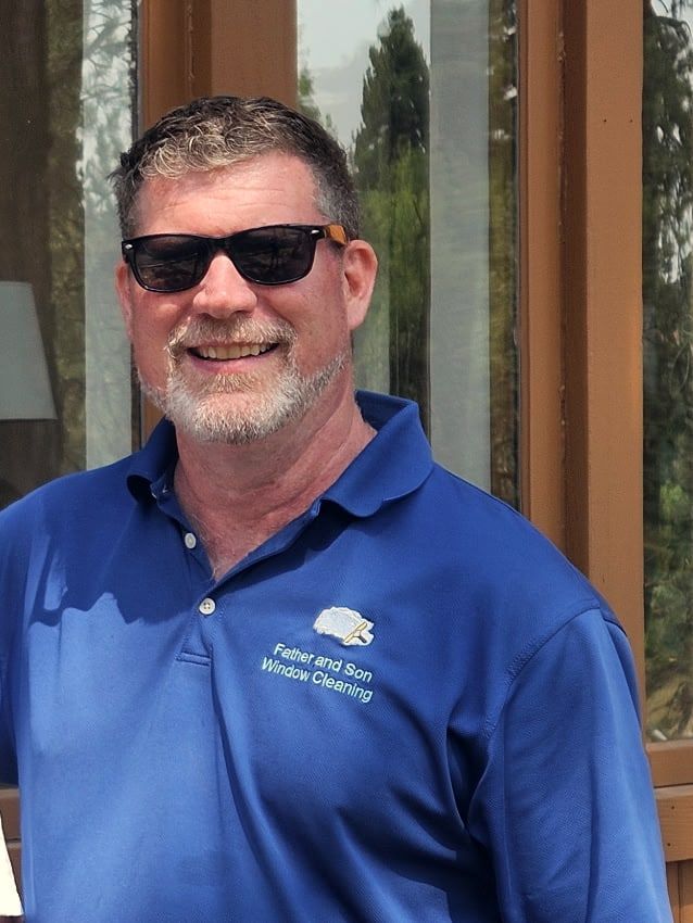Dan, owner and operator of Father & Son Window Cleaning, smiling outside a foothills home in a branded polo shirt and sunglasses.