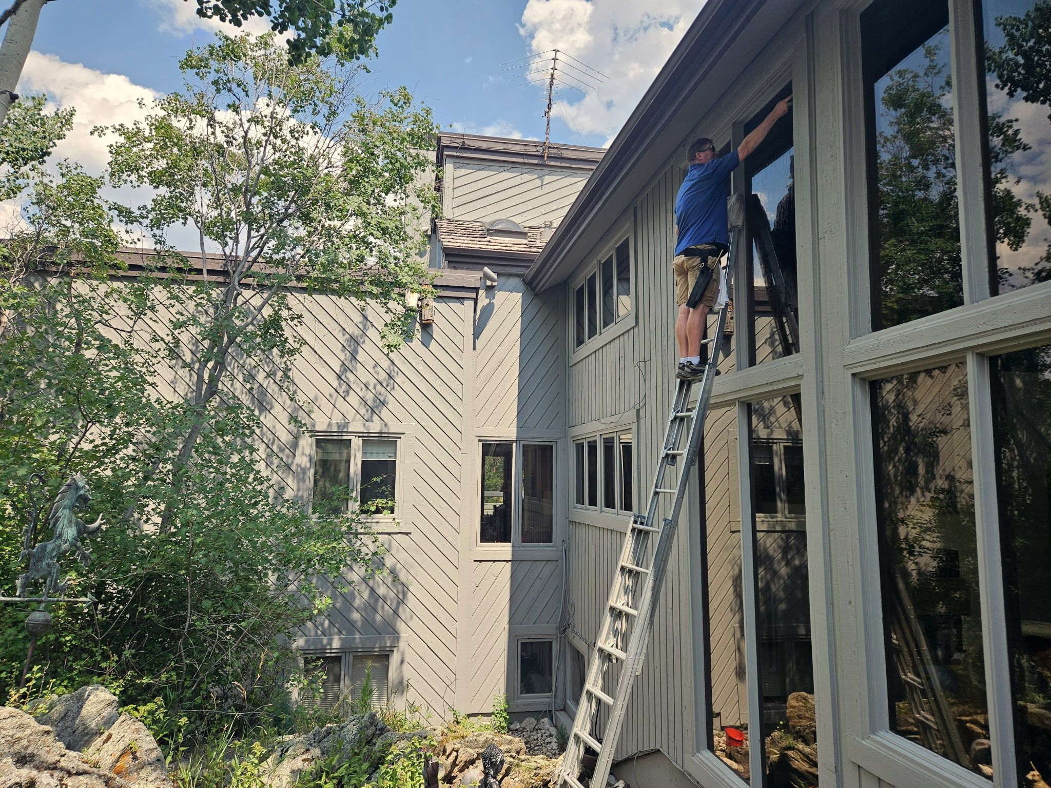 One of the crew on an extension ladder, squeegeeing the top of a tall window on a Front Range home with a wall of glass.
